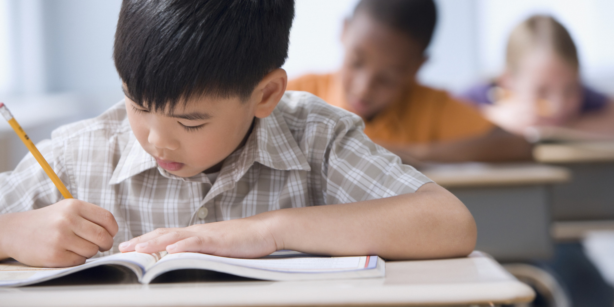 Asian boy writing in workbook in classroom